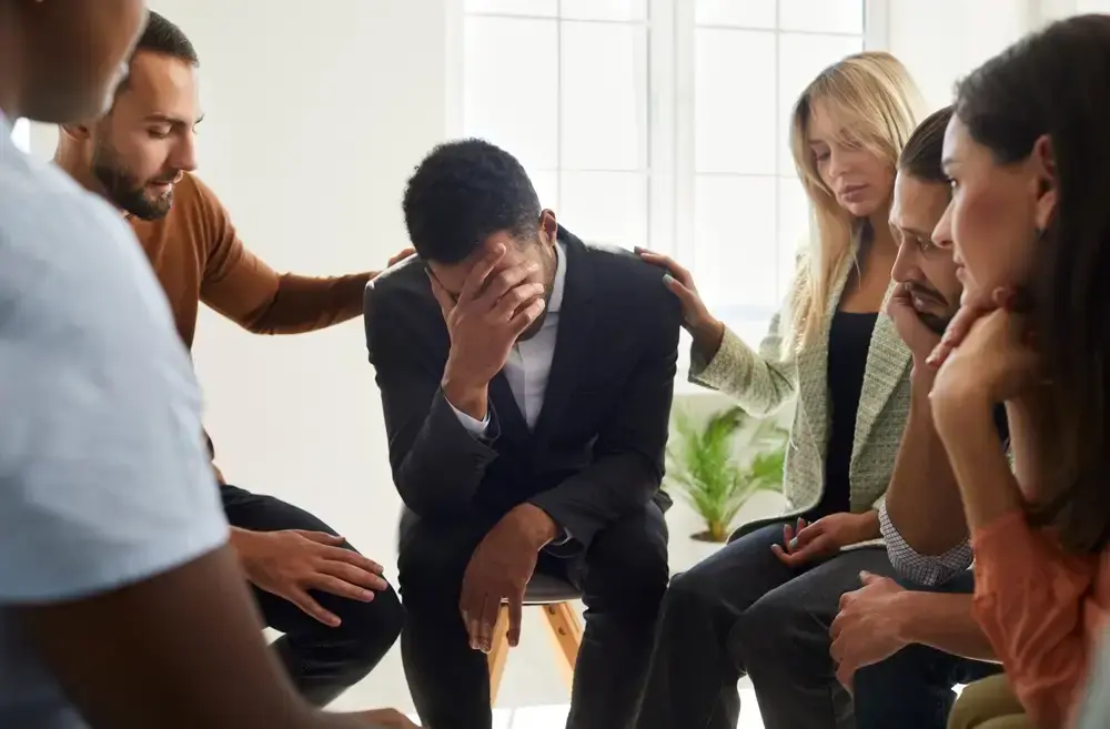 Six people sitting in a circle, some resting a hand on the person in the center.